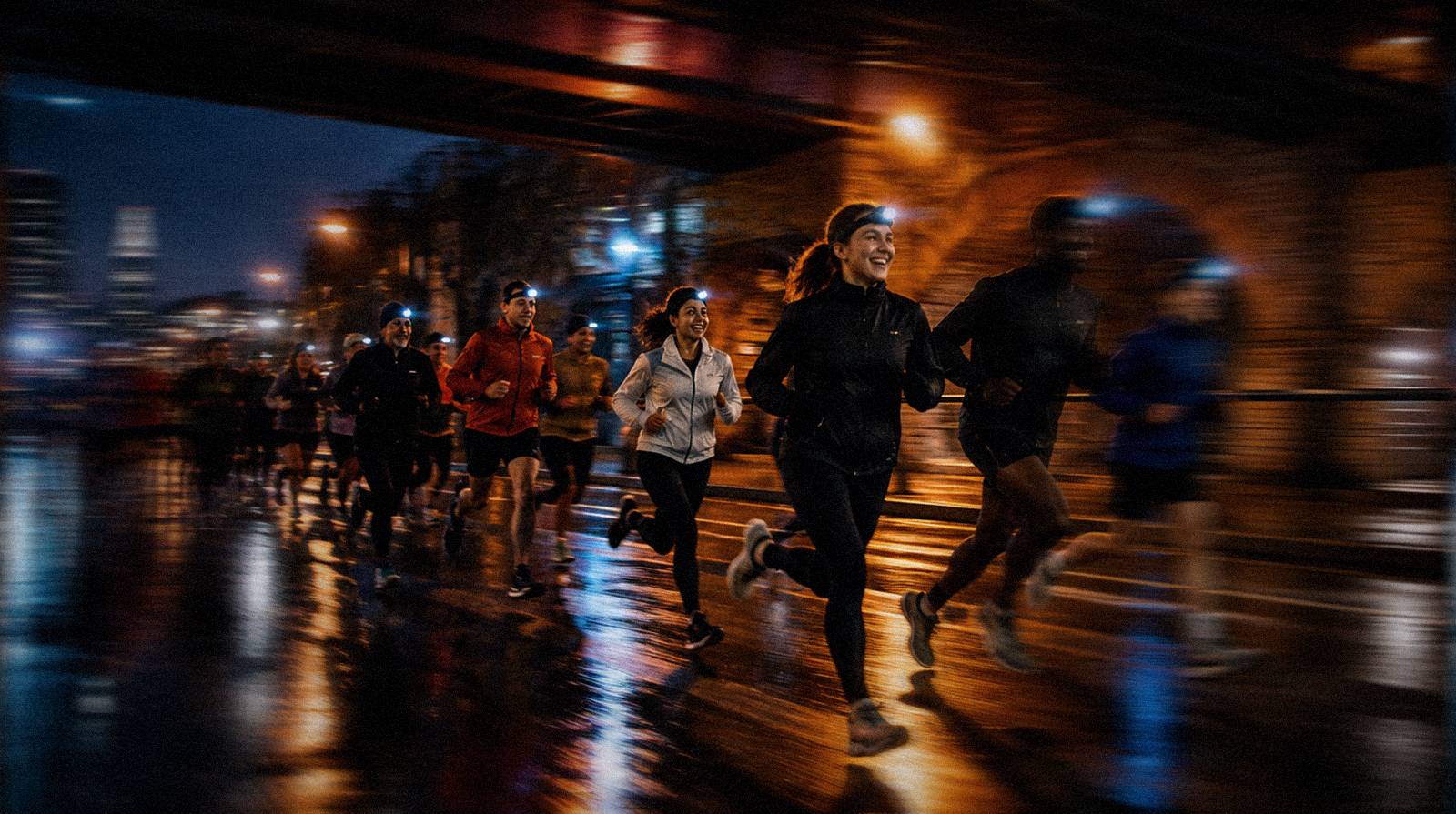 A run club setting off together under a railway bridge at night